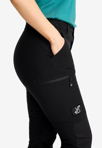 Svarta cargobyxor med en åtsittande design, som har en blixtlåsficka och en logotypapplikation. Tyget har en slät yta och har en lätt elasticitet.