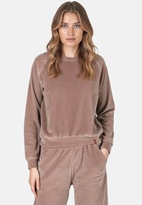 Felpa in velour marrone con maniche lunghe, scollo rotondo e polsini a costine. Texture morbida e vestibilità rilassata, abbinata a pantaloni coordinati.