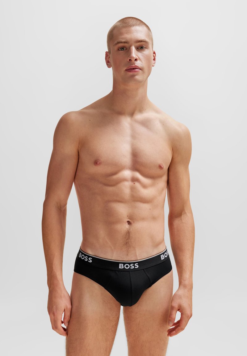Black cotton briefs with a white "BOSS" logo on the waistband, featuring a sleek, fitted design. Model shown with a neutral background.