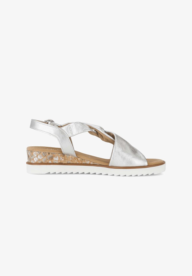 Sandalia de mujer de cuero plateado con tiras cruzadas, cuña de corcho, suela blanca con relieves y hebilla ajustable en el talón.