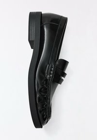 Mocassin en cuir noir avec un petit talon large et des détails cousus sur la tige, photographié sur un fond blanc uni.