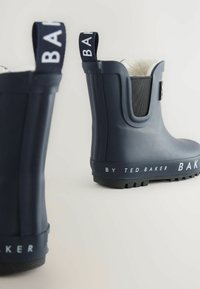 Bottes de pluie en caoutchouc navy avec un soufflet texturé, logo blanc sur une bande contrastante, et une semelle rainurée pour l'adhérence. Intérieur doublé.