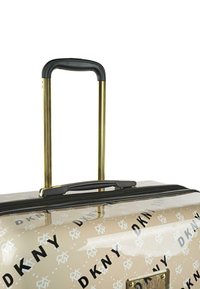 Maleta dura beige con acabado brillante, patrón de logo negro, mango telescópico dorado y cremallera negra. Acento metálico en la parte frontal.