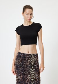 Schwarz gekürztes T-Shirt mit kurzen Ärmeln, kombiniert mit einem Rock im Leopardenmuster in verschiedenen Braun- und Cremetönen. Glatte Textur.