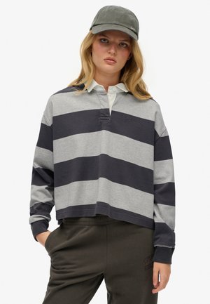 Grijs en marineblauw gestreept cropped rugbyshirt met een col en knoopsluiting, gecombineerd met donkere groene joggers.