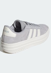 Grå mockaskor med en kraftig vit sula, med tre vita ränder, en vadderad krage och en präglad logotyp på hälen.