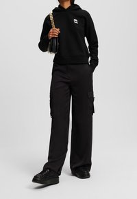 Czarna bluza z kapturem z małym logo, zestawiona z czarnymi spodniami cargo z kieszeniami oraz czarnymi teksturowanymi sneakersami na platformie.