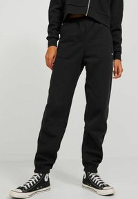 Black sweatpants made of soft fabric, featuring an elastic waistband, tapered cuffs, and a small logo detail on the front side.