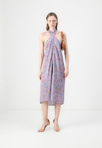 Halterneck-Midikleid in Helllila mit Blumenmuster, locker geschnitten und mit seitlichem Schlitz. Kombiniert mit transparenten High-Heel-Sandalen.