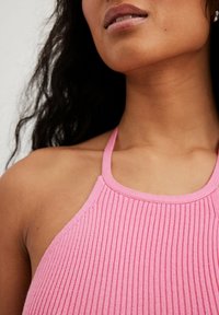 Roze geribd haltertopje met een ronde halslijn. De stof lijkt zacht te zijn, met een gestructureerd patroon en een aansluitende pasvorm rond de nek.