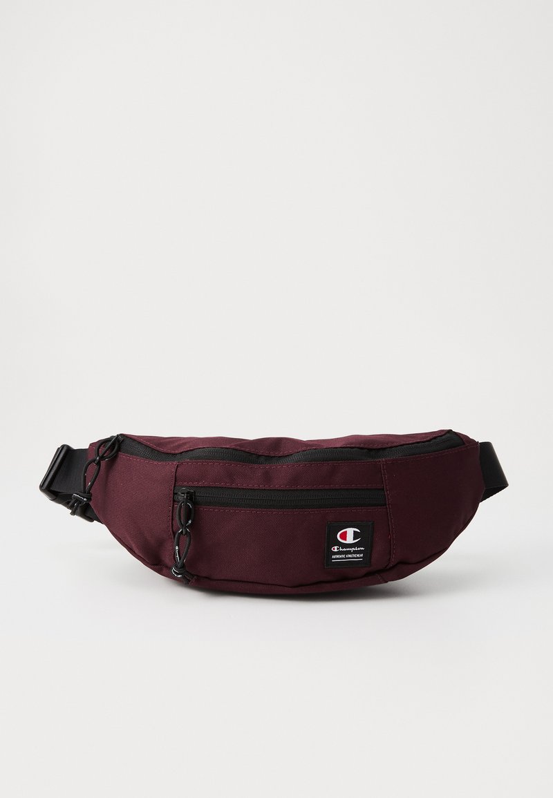 Sac banane bordeaux en tissu durable, avec une fermeture éclair noire, une sangle ajustable et un petit logo cousu sur le devant.