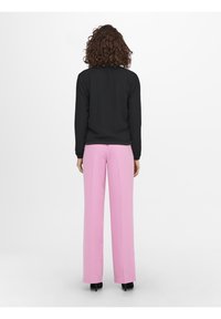 Zwarte langste mouwen top en roze wijde broekspijpen. De top heeft een fitted ontwerp; de broeken hebben een gladde textuur en een hoge taille.