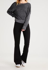 Svarta vida byxor i kombination med en mörkgrå ribbad tröja med vid halsringning och långa ärmar, tillverkad av ett strukturerat material.