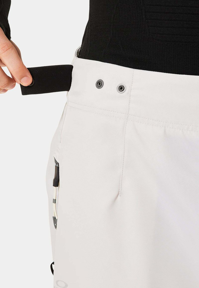 Weiße Hose mit strukturiertem Bund, ausgestattet mit einem schwarzen Riemen, Metallösen und einer seitlichen Tasche mit Kordelzug.