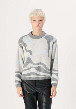 Jersey de punto gris y crema con patrones abstractos, cuello redondo y mangas largas. Llevado con pantalones de cuero negro texturizado.