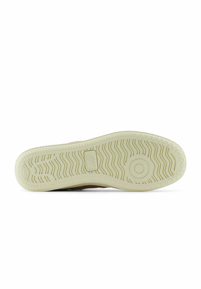 Suela de una zapatilla con una superficie de goma texturizada en un tono blanco roto, que presenta un patrón en zigzag y acentos circulares. Borde superior en color marrón claro visible.