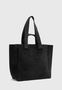 Sac fourre-tout noir en tissu texturé avec deux poignées robustes. Présente un logo en relief sur le devant, de forme rectangulaire et une apparence douce.