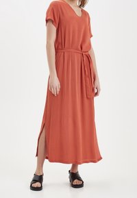Midi šaty v rezavé barvě s výstřihem do V, krátkými rukávy, látkovým páskem, postranními rozparky a hladkým povrchem. V kombinaci s černými sandály.