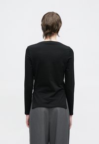 Μαύρο τοπ με μακριά μανίκια, εφαρμοστή σιλουέτα, στρογγυλή λαιμόκοψη και λεία υφή, συνδυασμένο με φαρδιά γκρι παντελόνια.