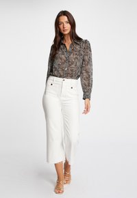 Zwart-witte blouse met patroon, een kraag, lange mouwen en knoopsluiting; gecombineerd met witte hooggetailleerde cropped pants met een franjeszoom.