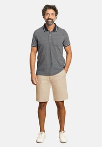 Polo de hombre de manga corta en patrón de cuadros navy con cuello y puños en contraste, combinado con pantalones cortos beige y zapatillas blancas.