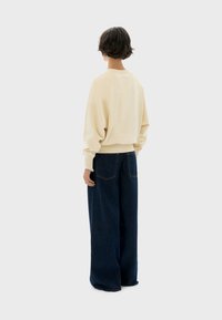 Beige knitted sweater with a relaxed fit and raglan sleeves, paired with wide-leg dark denim jeans featuring back pockets.