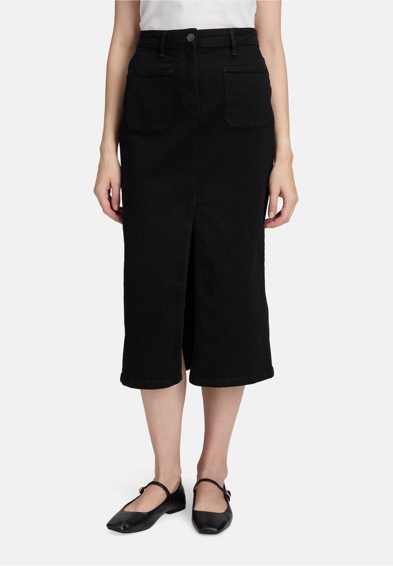 Femme portant une jupe midi noire avec des poches avant et une fente à l'avant, assortie à des ballerines Mary Jane noires et un haut blanc.