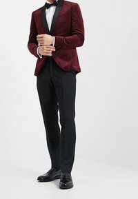 Burgundowa aksamitna marynarka z satynowymi klapami zestawiona z czarnymi spodniami i butami. Koszula jest biała, uzupełniona czarnym muszkietem.