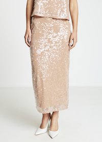 Zweiteiliges Pailletten-Set in sanftem Beige, bestehend aus einem bauchfreien Oberteil und einem langen Rock. Die Pailletten fangen das Licht ein und erzeugen einen schimmernden Effekt. Weiße High Heels.