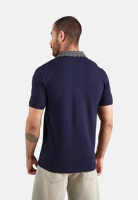 Camisa polo azul marino con un cuello estampado, mangas cortas y una textura sutil. La vista trasera muestra un ajuste entallado y un diseño limpio.