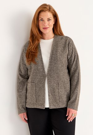 Harmaa neule cardigan, jossa on avonainen etuosa, kaksi etutaskua, pitkät hihat ja tekstuuripinta, kerrostettuna valkoisen paidan päälle.