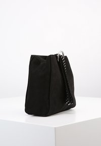 Svart mockaväsk med en strukturerad form, som har ett vävt handtag och metallbeslag. Slät textur med en mjuk, matt yta.