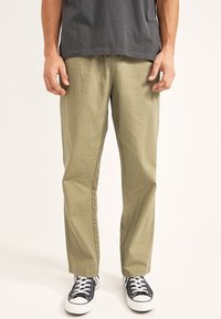Pantalones khaki de pernera recta, hechos de un tejido ligero. Presentan costuras laterales y un corte relajado. Combinados con zapatillas negras y blancas.