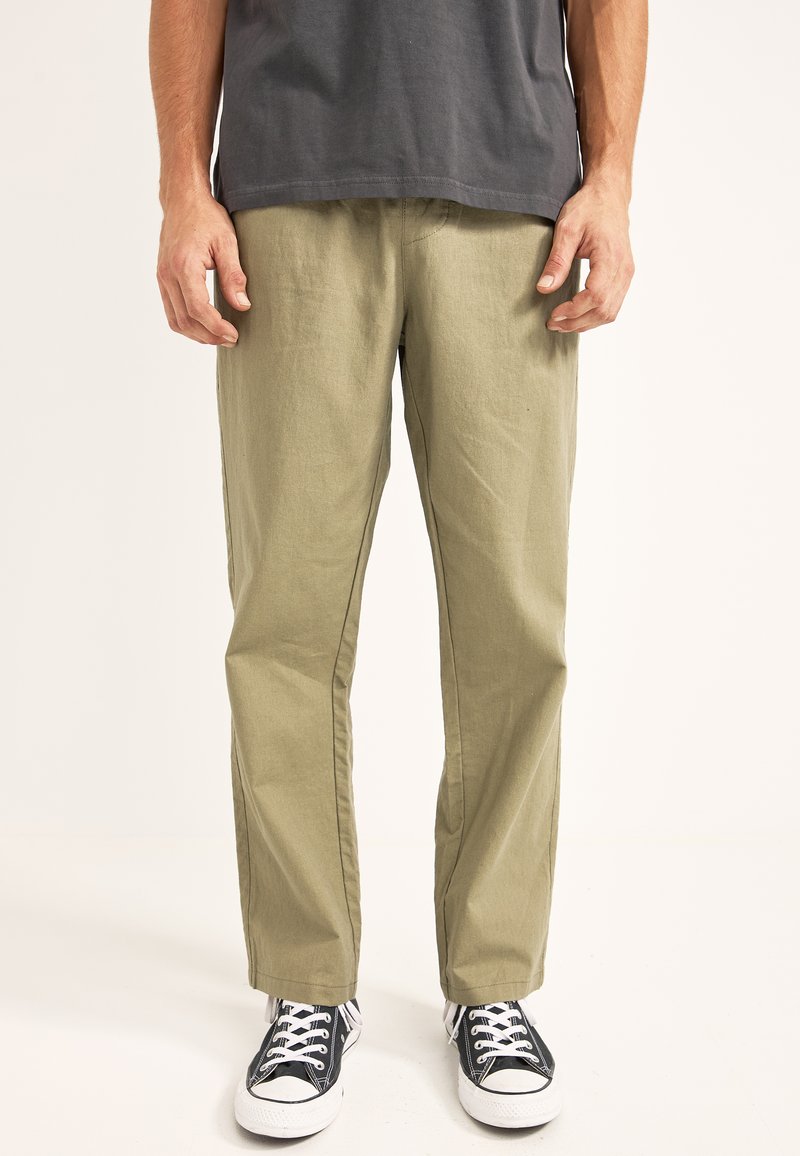 Pantalones khaki de pernera recta, hechos de un tejido ligero. Presentan costuras laterales y un corte relajado. Combinados con zapatillas negras y blancas.