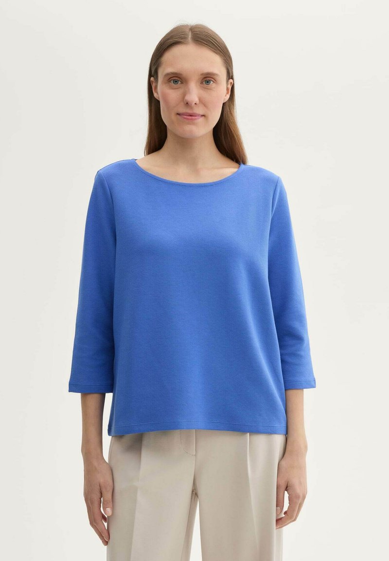 Blaues Baumwollmischungsoberteil mit rundem Ausschnitt und Dreiviertelärmeln, das eine strukturierte Oberfläche und eine lockere, entspannte Passform aufweist.