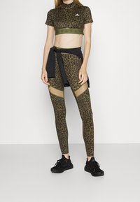 Conjunto deportivo que presenta un top corto ajustado de estampado de leopardo en color caqui y leggings a juego con detalles de malla, complementados con zapatillas negras.