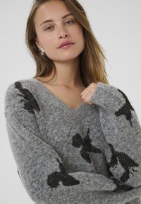 Maglione grigio, soffice a maglia con scollo a V e motivi astratti neri. Maniche lunghe e ampie con una finitura morbida e Texturizzata.