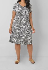 Svart och vit blommig A-linje klänning med V-hals, korta ärmar och strukturtyg. Bärs med bruna randiga slip-in sandaler.