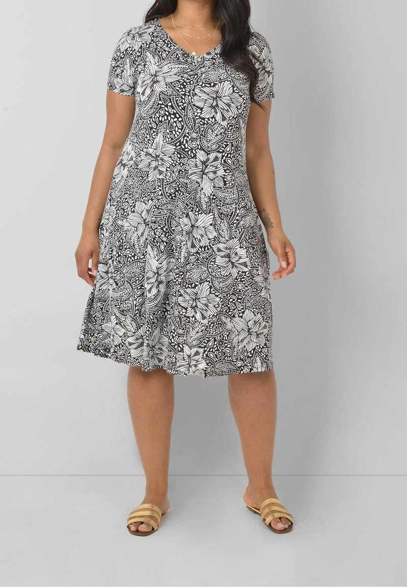 Svart och vit blommig A-linje klänning med V-hals, korta ärmar och strukturtyg. Bärs med bruna randiga slip-in sandaler.