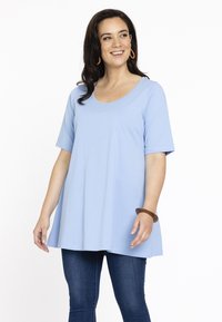 Lyseblå tunika med korte ærmer, rund halsudskæring og en løs pasform. Kombineret med mørkeblå jeans. Glat tekstur.