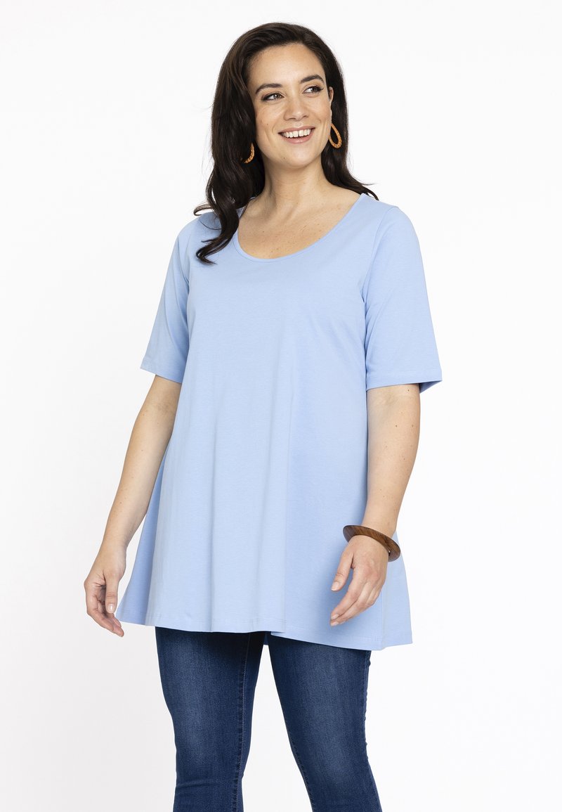Lyseblå tunika med korte ærmer, rund halsudskæring og en løs pasform. Kombineret med mørkeblå jeans. Glat tekstur.