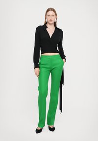 Haut court noir à manches longues, associé à un pantalon taille haute vert vif. Les chaussures sont des ballerines noires à bout pointu.
