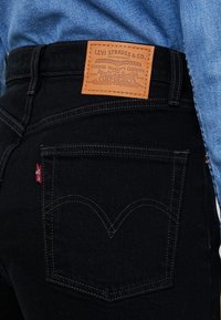 Zwarte spijkerbroek met een leren label waarop "Levi Strauss & Co." staat op de achterkant, voorzien van het standaard ontwerp met vijf zakken en contrasterende stiksels.