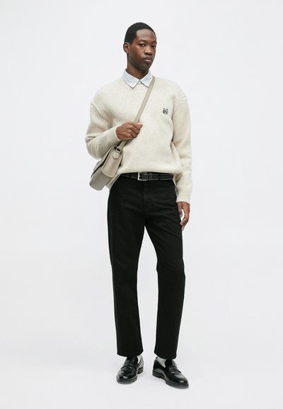 Bežs džemperis ar mazu logo, svītrainā krekla apkakle, melni bikses, melnas kurpes un pelēks pleca soma. Vienkāršs un mūsdienīgs dizains.