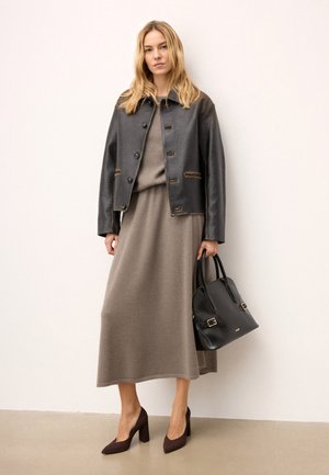 Veste en cuir noire avec des coutures visibles, superposée sur une robe grise. Des chaussures à talons bruns et un sac à main noir complètent le look.