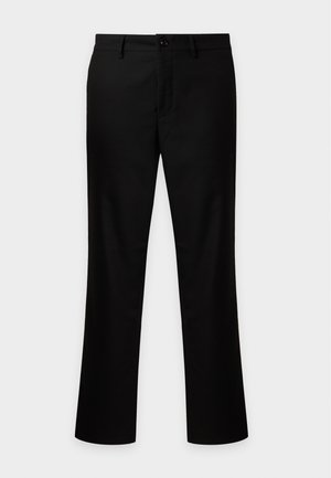 Homme portant un pull duveteux violet clair, un pantalon noir et des baskets blanches, debout devant un fond blanc uni.