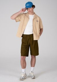 Button-up shirt with orange and white stripes, white t-shirt, brown shorts, blue cap, and gray sneakers with white socks.