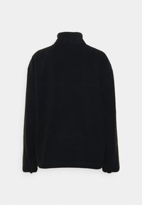 Pull-over en polaire noire avec un col montant, des manches longues et un design simple. Présente une couture horizontale à travers le dos. Texture douce.