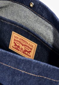 Tmavě modré džíny z denimu s světle modrou podšívkou. Obsahují béžovou koženou nášivku s červeným textem a designem koní a nýtků.