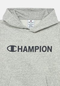 Sudadera gris hecha de una tela suave con un bolsillo tipo canguro en la parte frontal. Presenta un gran logo "CHAMPION" en un gris oscuro en el pecho.